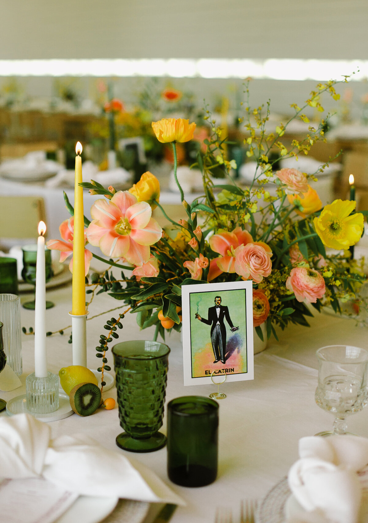 Wedding reception table decorated with peach and yellow florals, green glasses and yellow candles