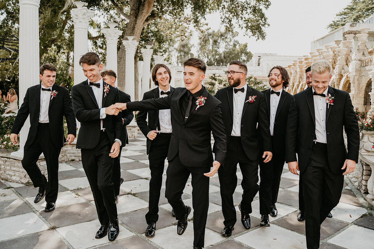 groomsmen walking and laughing in tuxedos at the kapok tree clearwater florida