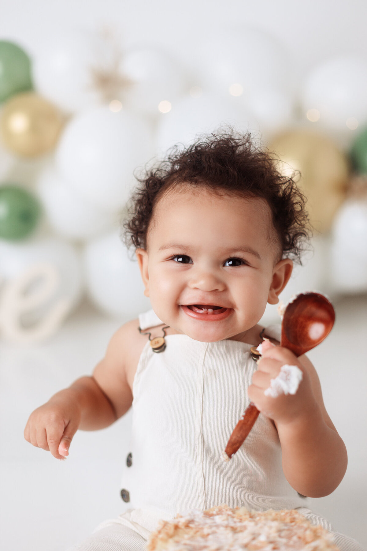 smiling one year old smashing birthday cake with wooden spoon