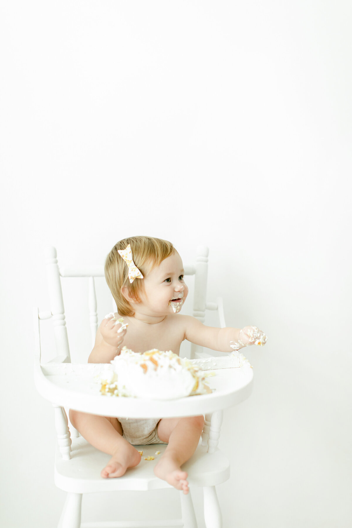 girl in high chair wearing bow smashing cake