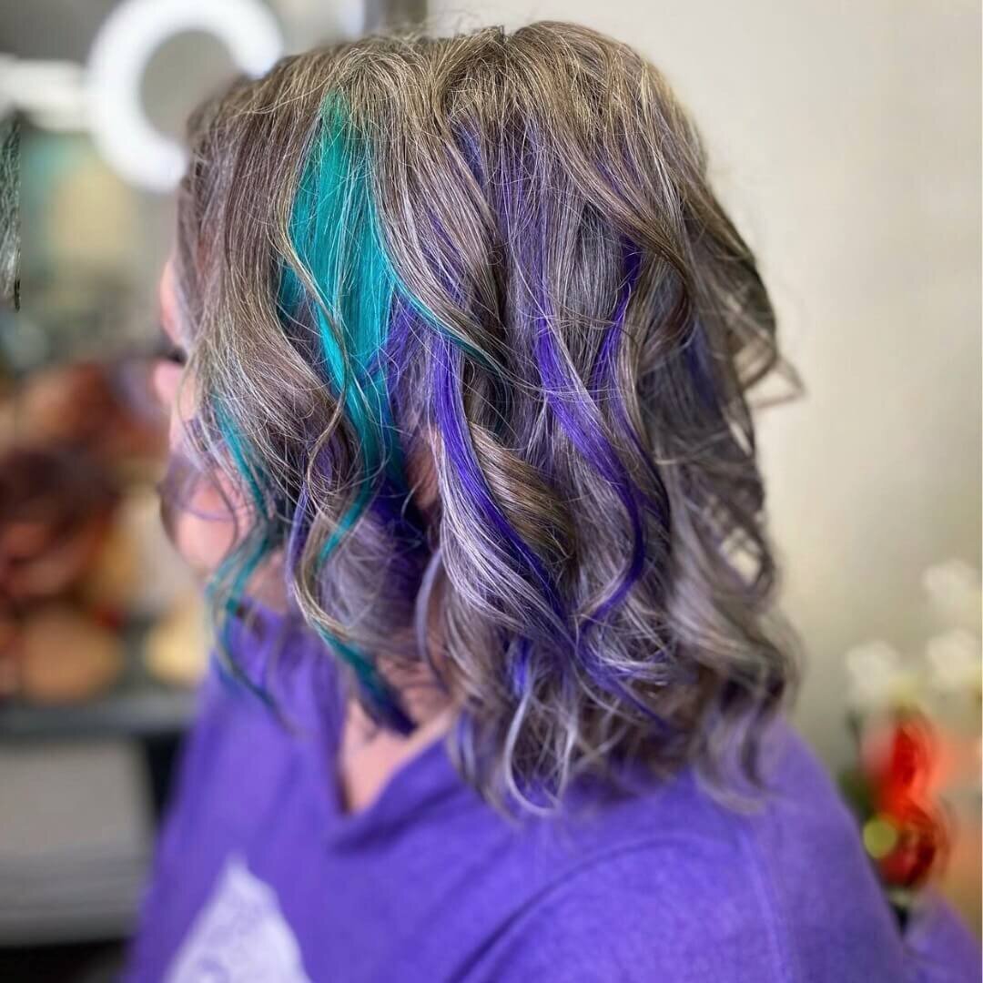 A woman with shoulder-length hair featuring vibrant blue and purple highlights, showcasing a bold and creative hairstyle created by 212 Salon, Spa, & Barbershop.