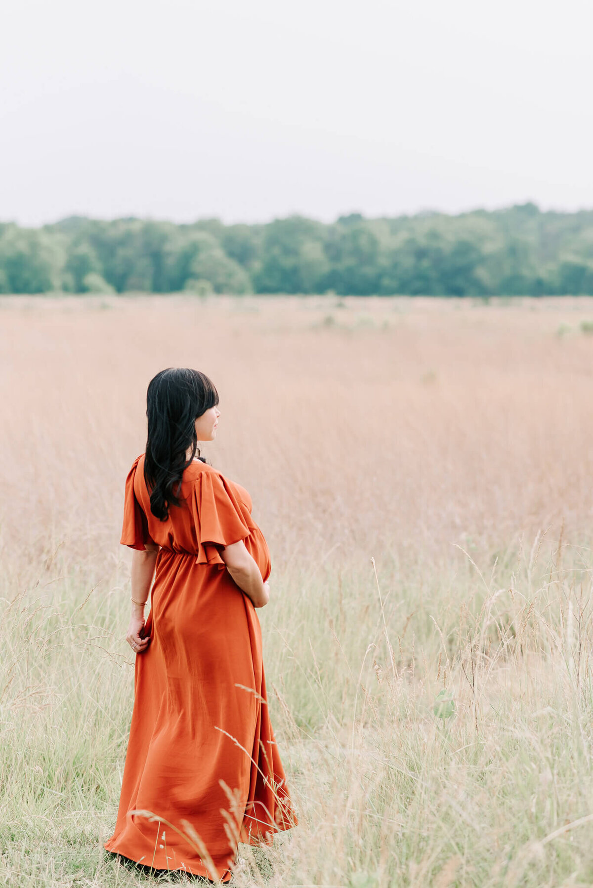 An expecting black-haired woman walking into the grass by a Northern Virginia maternity photographer