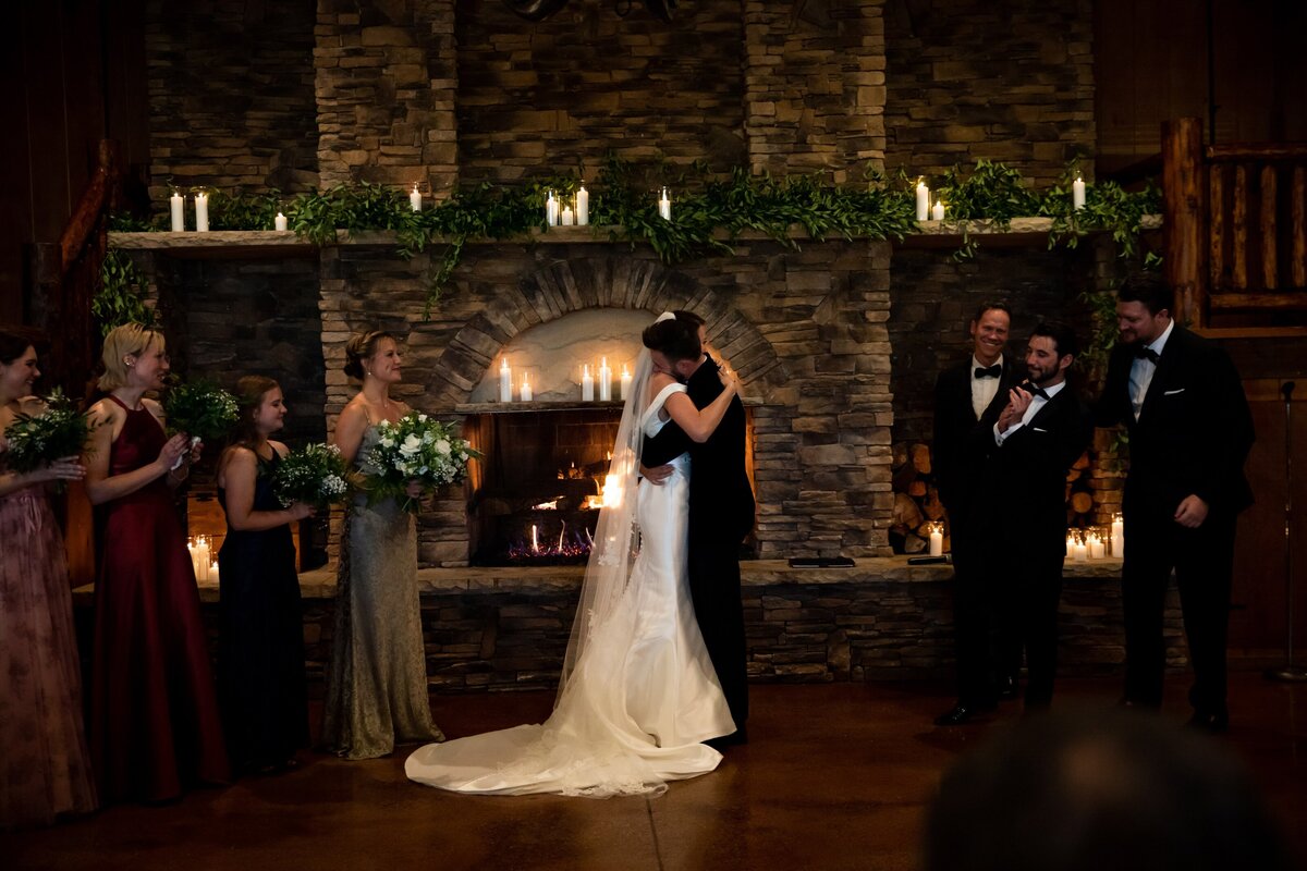 Bride and Groom share an embrace in front of a fireplace with greenery and candles at Spruce Mountain Ranch.