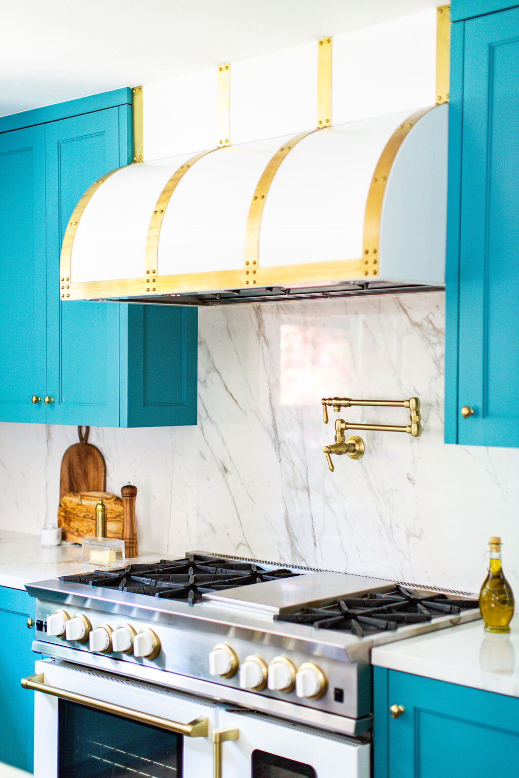 Kitchen with Teal cabinets, marble backsplash, and white and brass Blu Star range and hood.