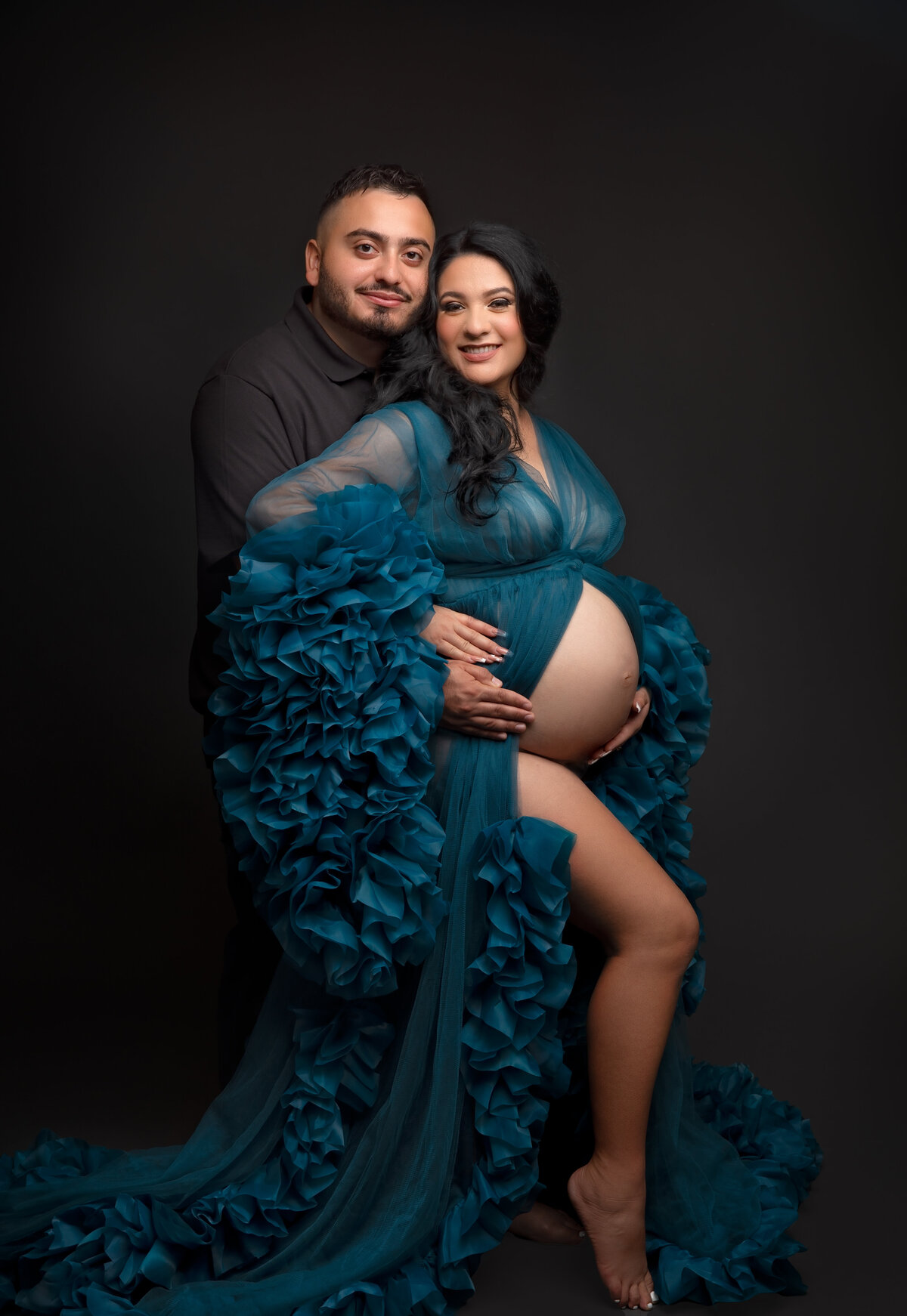 A radiant mom-to-be poses in an elegant designer gown with partner, capturing the unique beauty of her pregnancy journey at Little Legacies Studio.