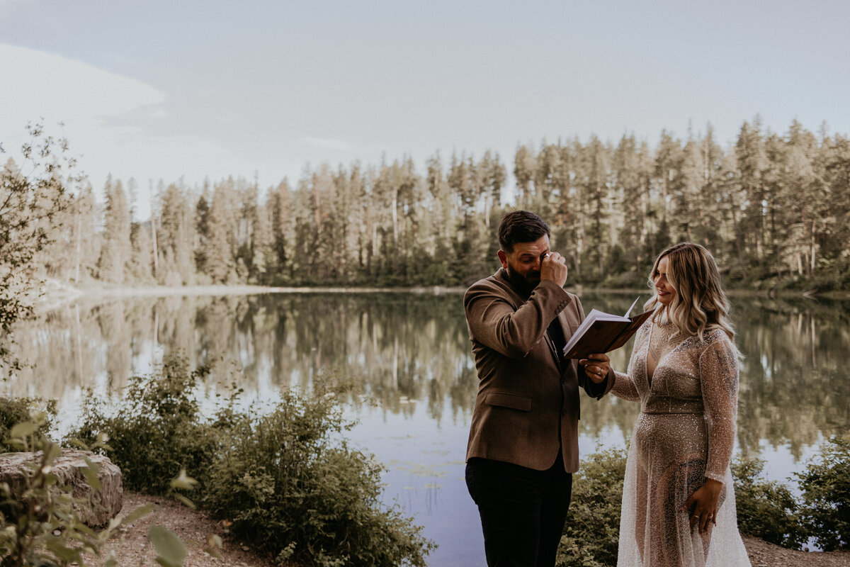 bride and groom reading vows to each other in front of a lake