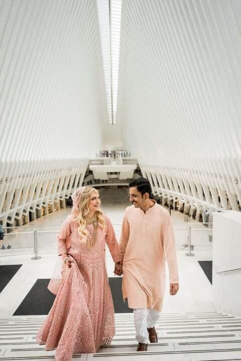 Engaged couple walking hand in hand at the Oculus in NYC, dressed in coordinating peach outfits during their modern engagement session.