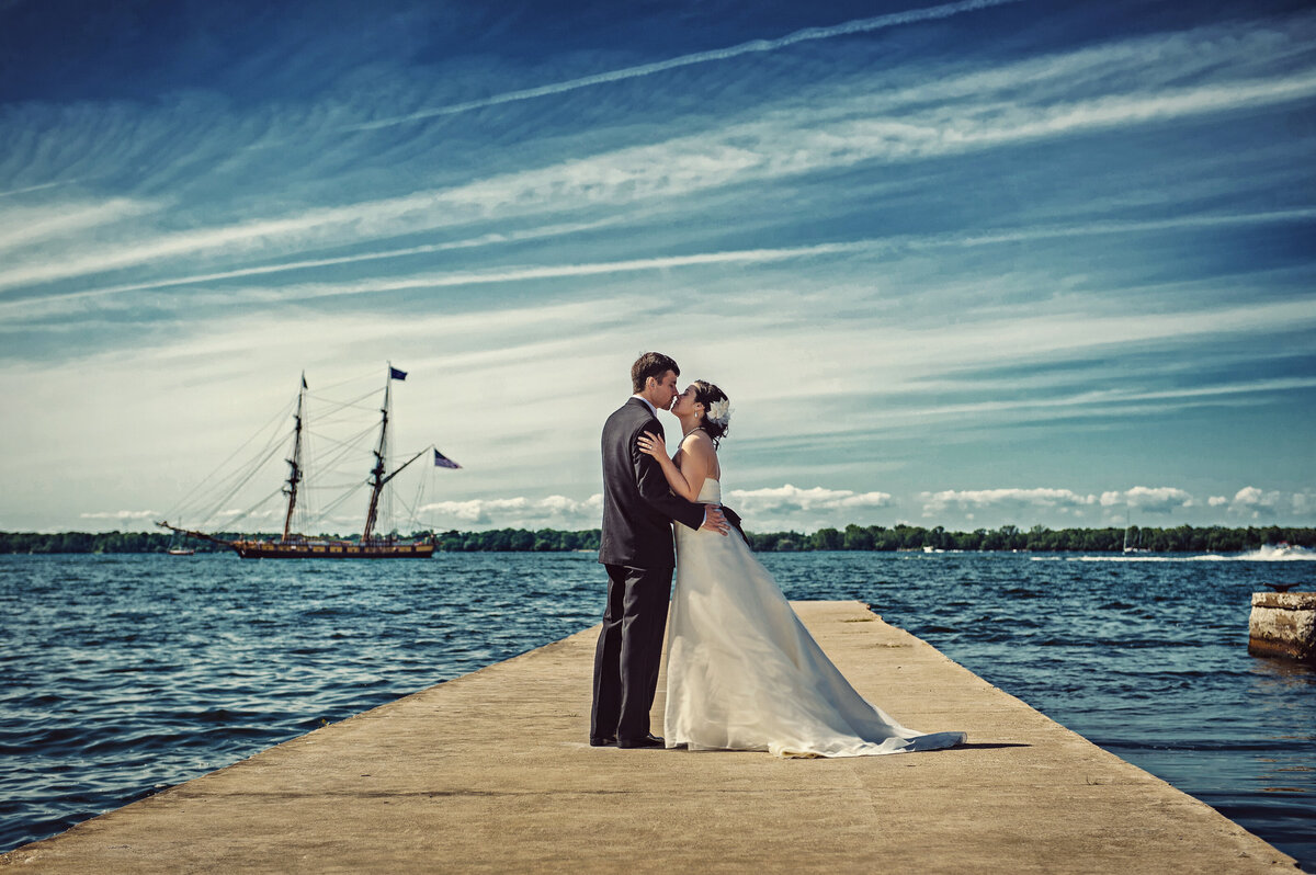 Bride and Groom kissing on a pier with the US Brig Niagara sailing in the background.