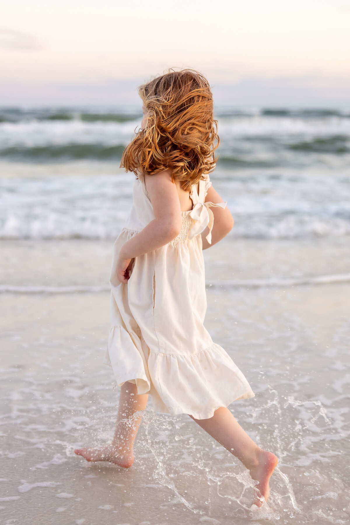 little girl with red hair and cream dress running away on the beach on 30a.