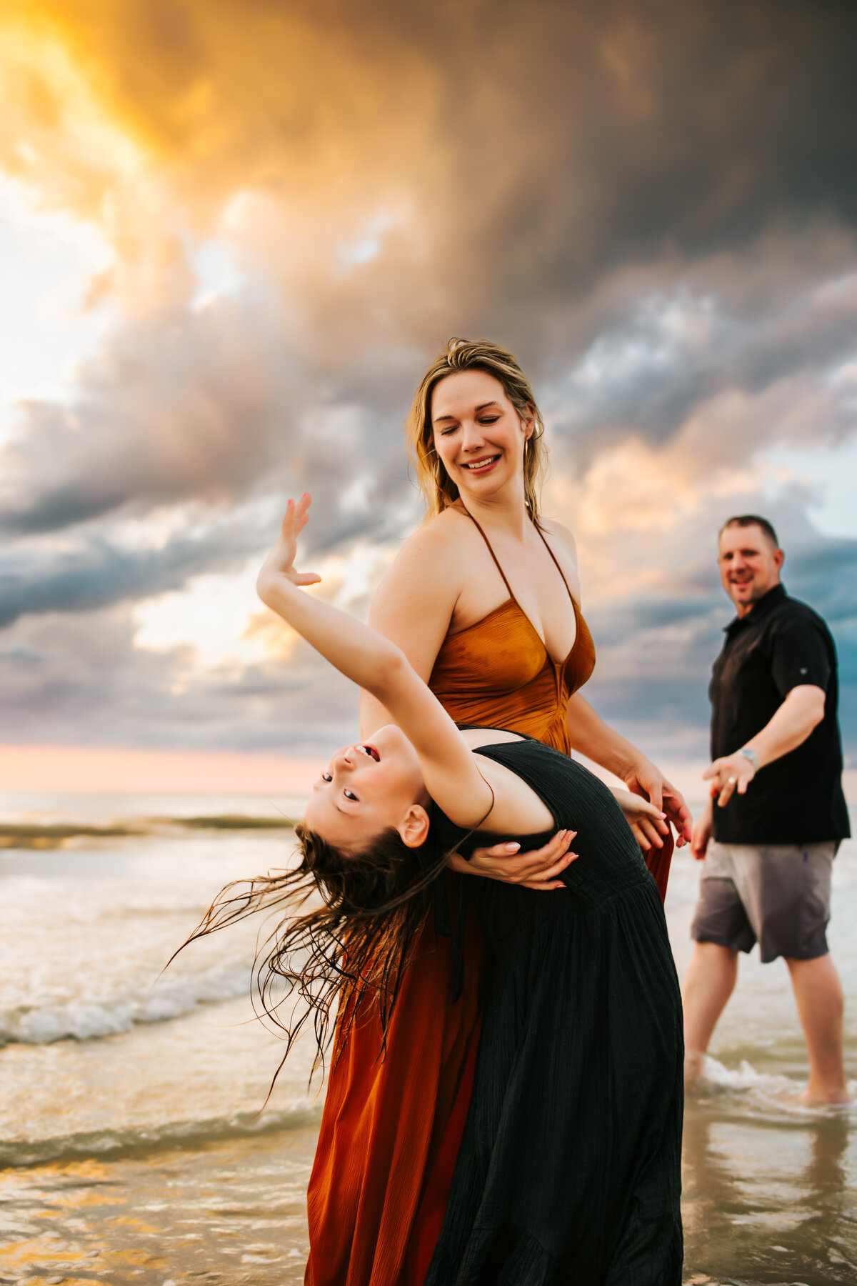 fin family portrait of a mom and her daughter dancing in the water during a beach vacation photo shoot