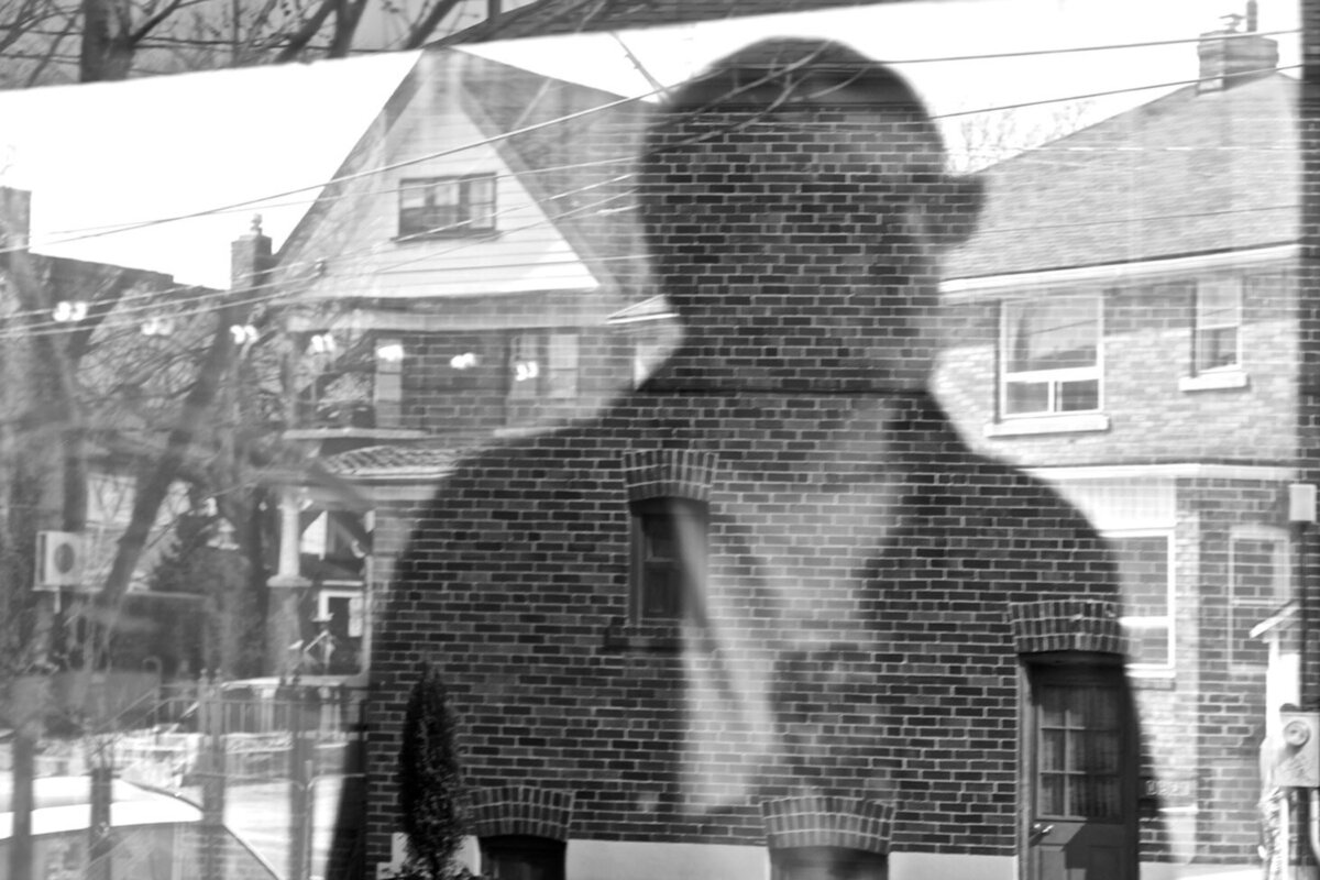 Music Artist portrait black and white reflection of Mikey Manvil in window looking at brick houses while wearing sunglasses Reflections Gallery