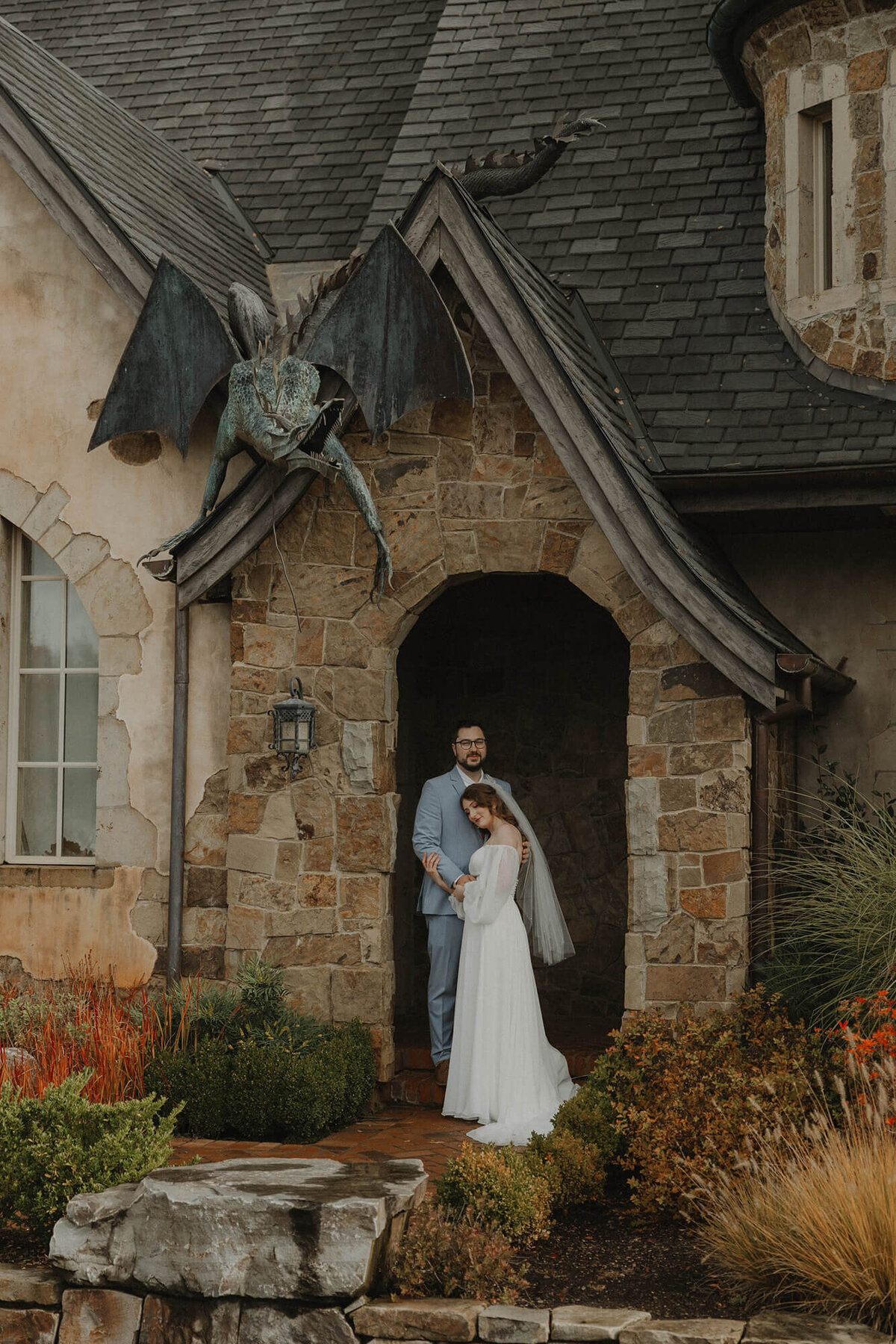 A bride and groom standing in a doorway opening at the Chateau wedding venue with a gargoyle statue handing off the wall.