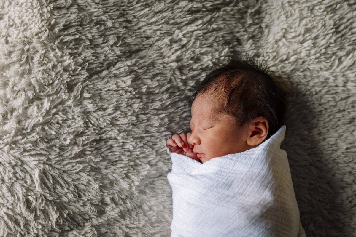 newborn in white swaddle sleeping on side on textured gray blanket