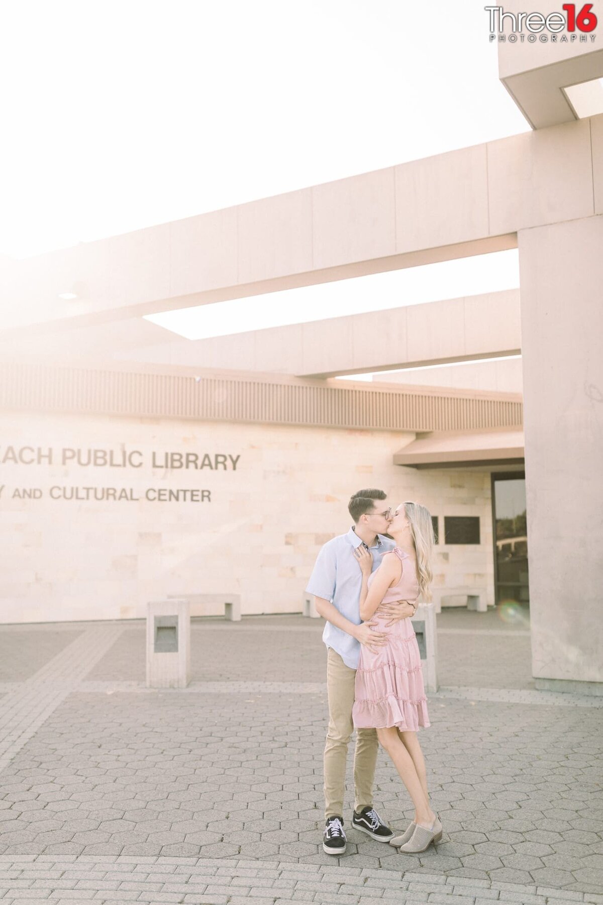 Engaged couple share a kiss at the entrance of the Huntington Beach Library