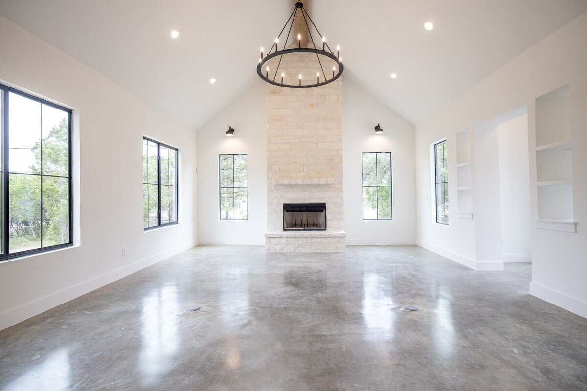 vaulted ceiling living room with limestone fireplace, concrete floors, black windows and farmhouse light
