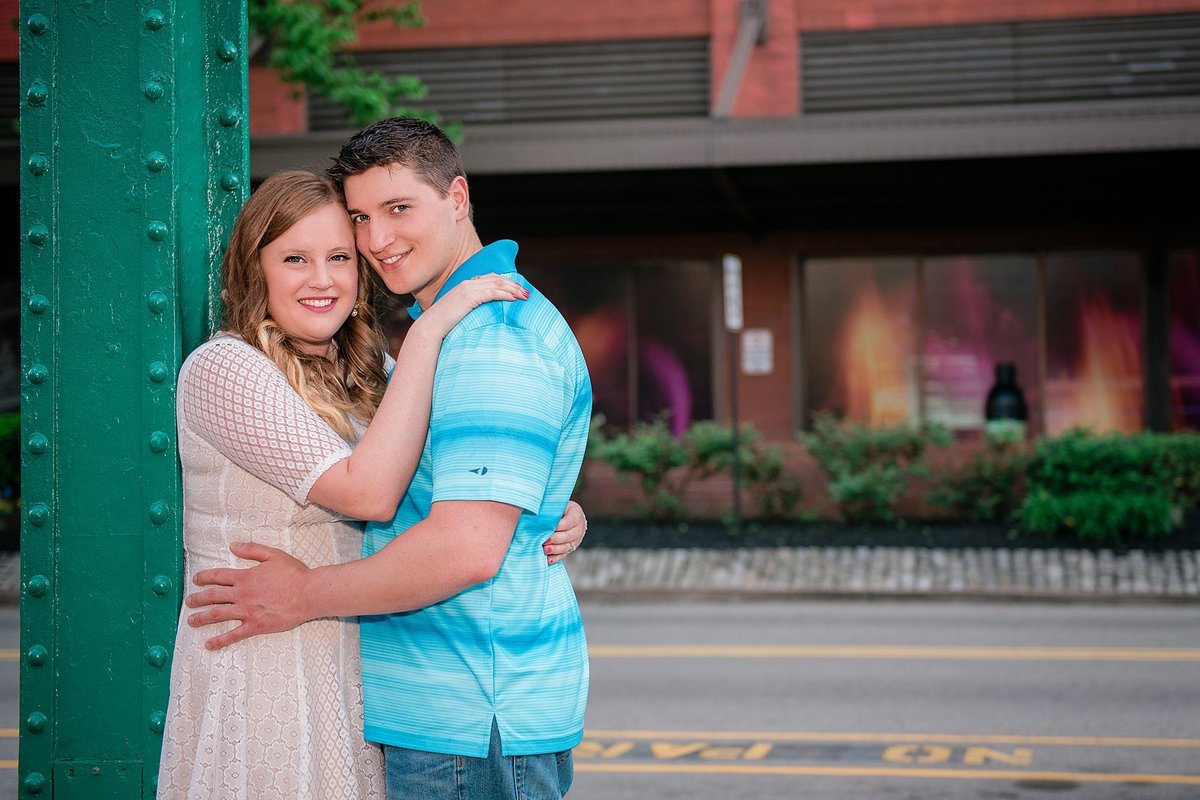 Engaged couple leaning against a green light post during their engagement session at Station Square in Pittsburgh, PA