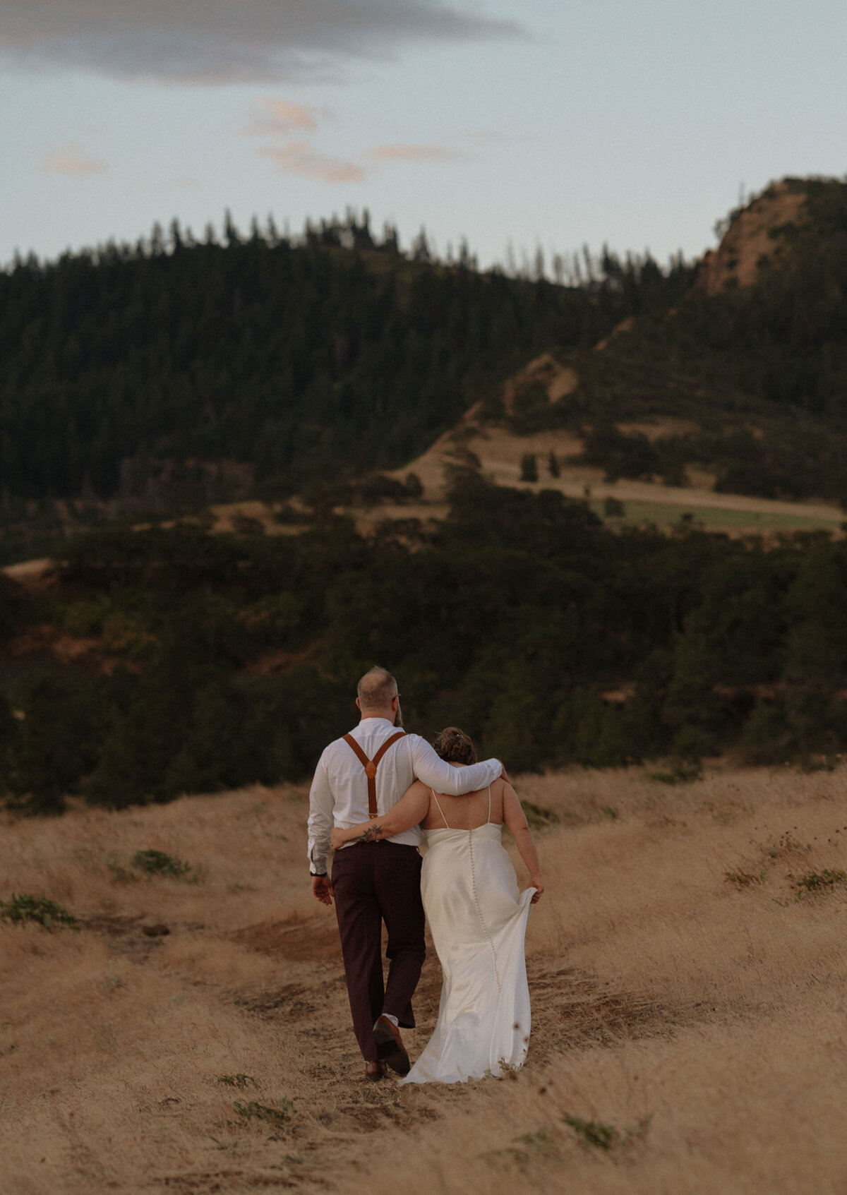 bride and groom embrace each other as they walk off into the distance among a grassy field after their elopement ceremony