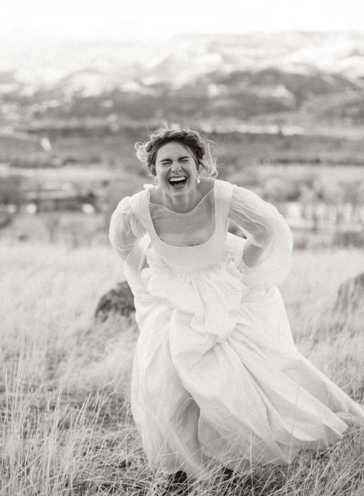Whimsical bride in flowy wedding dress running and laughing with mountains in the background