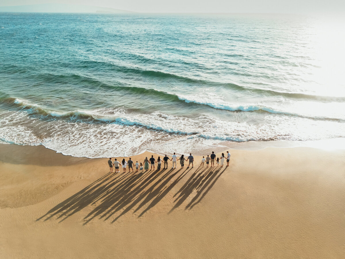 Maui Family Photographers capture family standing on beach together while drone captures aerial shot during family beach photos