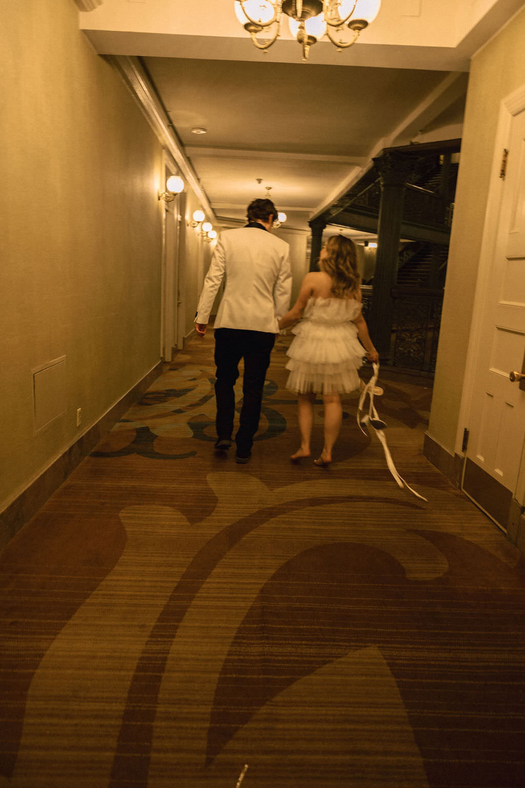 A newlywed couple walking down a hotel hallway together.