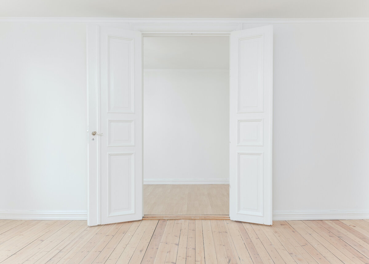 White doors are opened in blank white room with natural wooden floors.