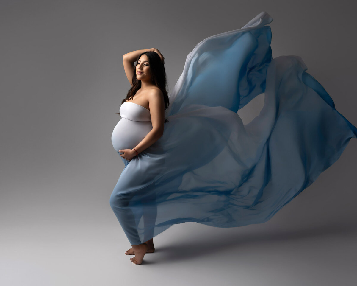 Dramatic maternity portrait in flowing blue dress captured by Austin maternity photographer with professional studio lighting
