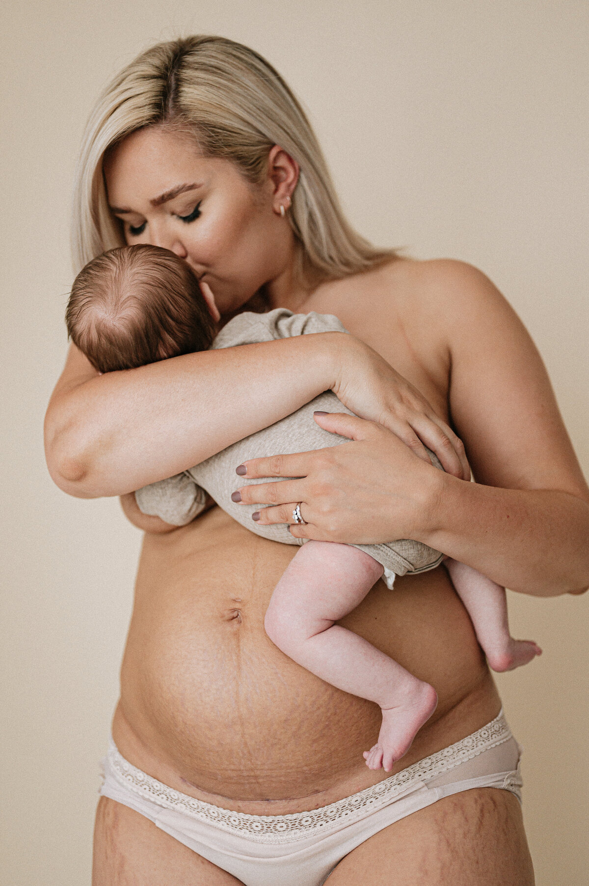 New postpartum mother with c-section scar kisses her newborn baby during a photoshoot near Bristol