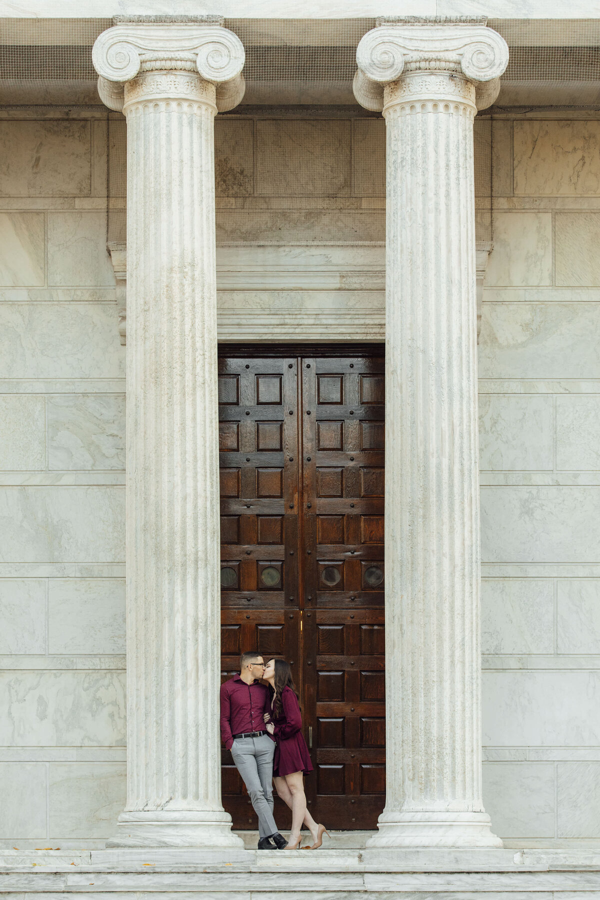 Couple kissing by building columns during engagement shoot in Princeton New Jersey