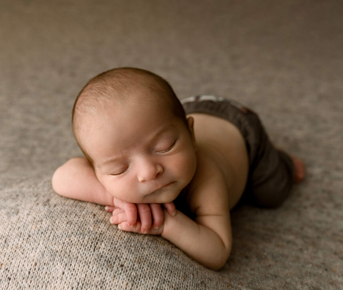 Photo of a newborn boy laying chin on hands in a photography studio