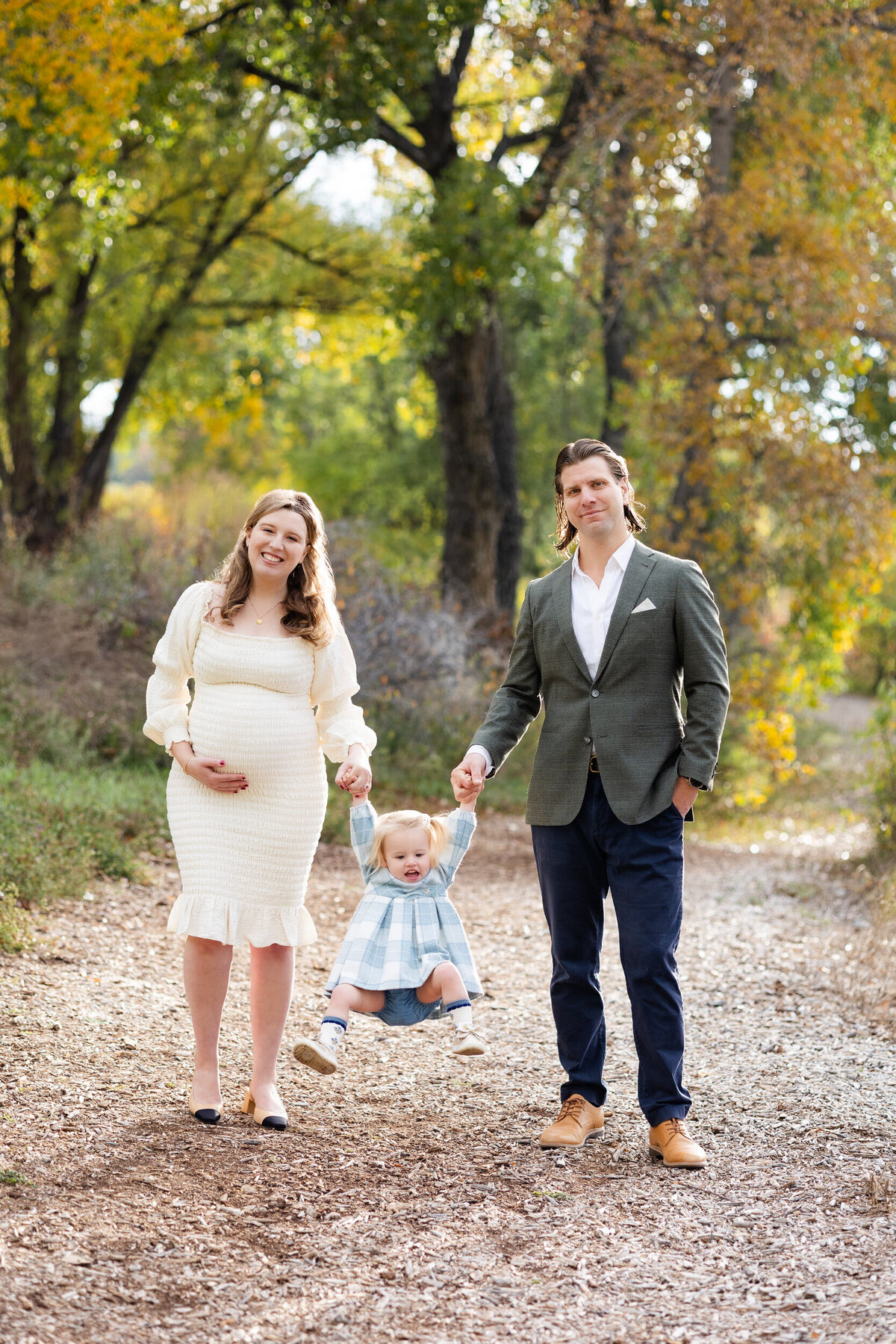 Mom and dad swing their toddler girl between them and they all smile at the camera.