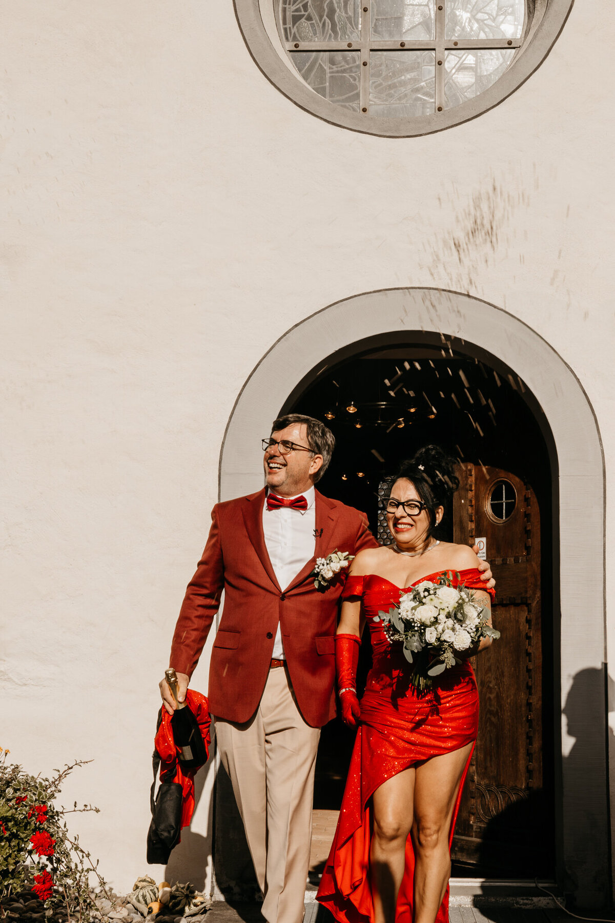 Een vrolijk moment van een bruidspaar dat samen de ceremonie afsluit, met rode accenten in hun outfits.