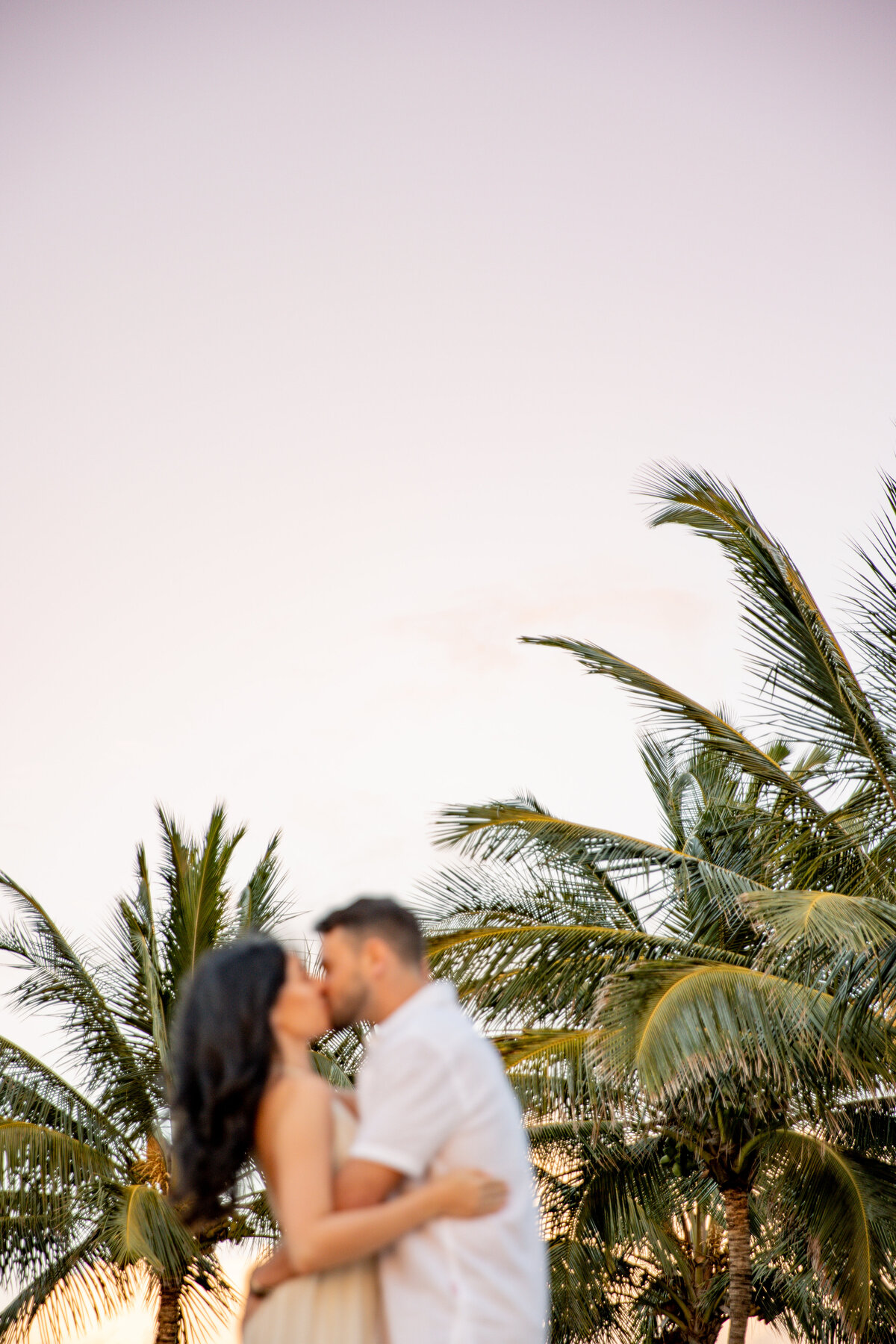 Maui Couples Photographer captures couple kissing in front of palm trees during beach engagement photos