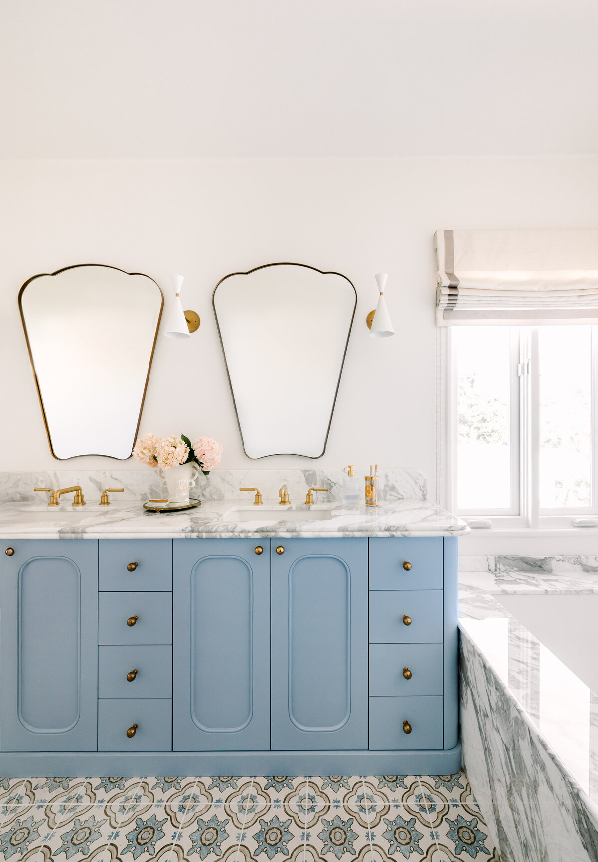 Primary bathroom with a custom vanity in Sherwin Williams Lakeside and rounded edges, Arabescato Corchia marble counters, Italian shield mirrors, Blueprint Lighting Monolith Wall Sconce, patterned floor tile, and a built in marble tub.