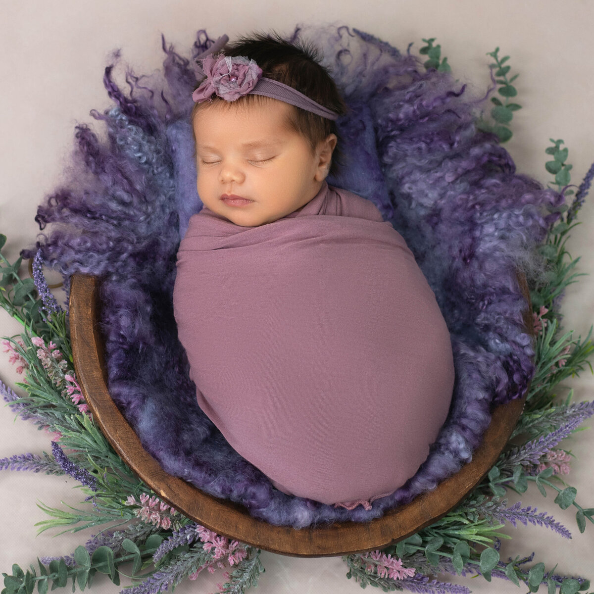 newborn girl in purple wrap surrounded by flowers