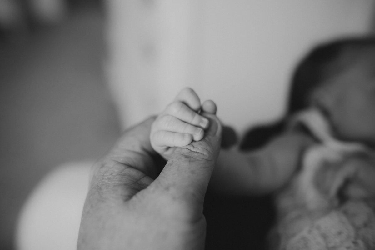 A close-up black and white image of a baby holding an adult's finger, creating a tender connection.