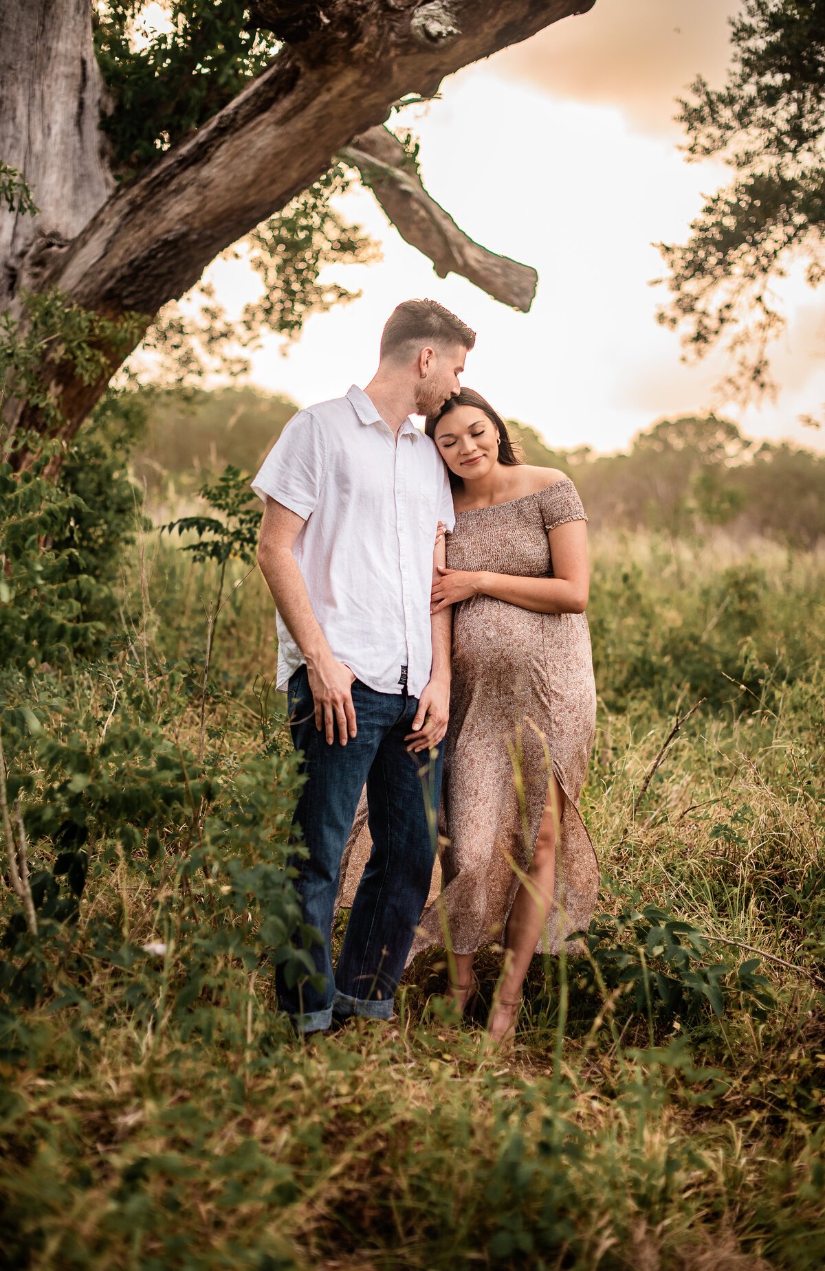 A mom and dad to be from Galveston county stand closely in a field.