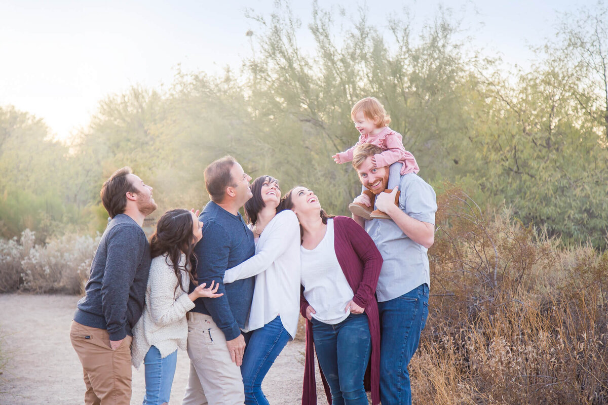 Couple and adult children at desert park looking up at laughing redheaded toddler