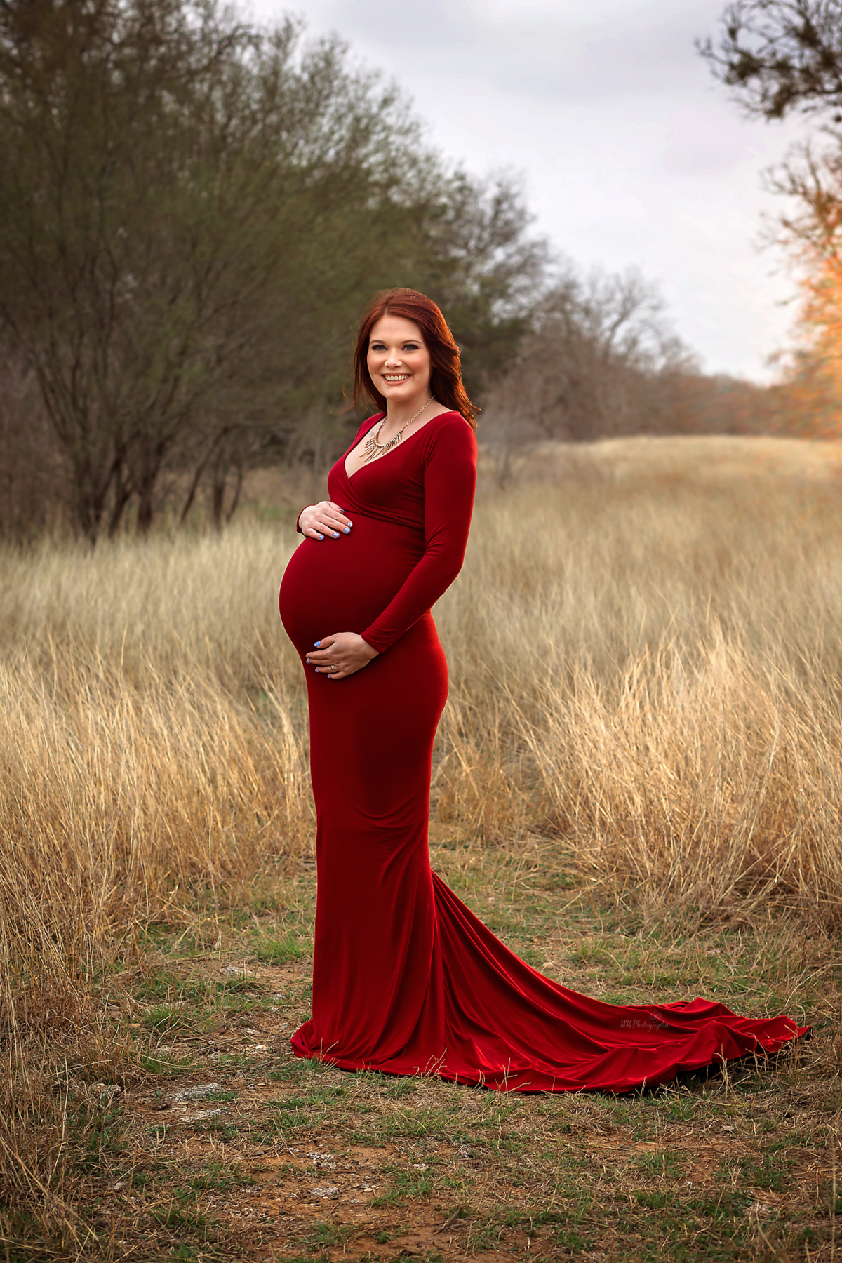 Radiate glamour in a styled winter maternity session near San Antonio. Our mom-to-be, draped in a scarlet flying dress, brings radiance and sophistication to the winter field setting.