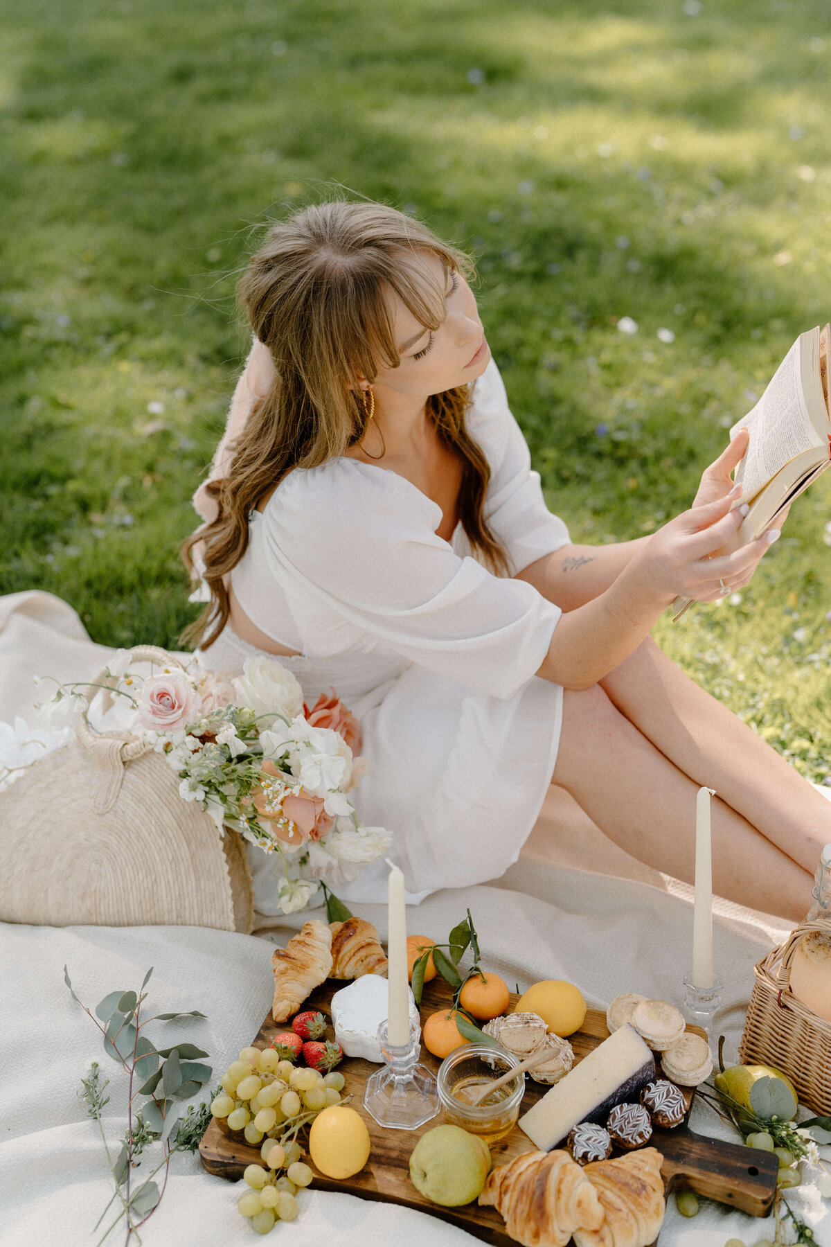 bride sitting reading with a board of fruit, cheese, florals and candles
