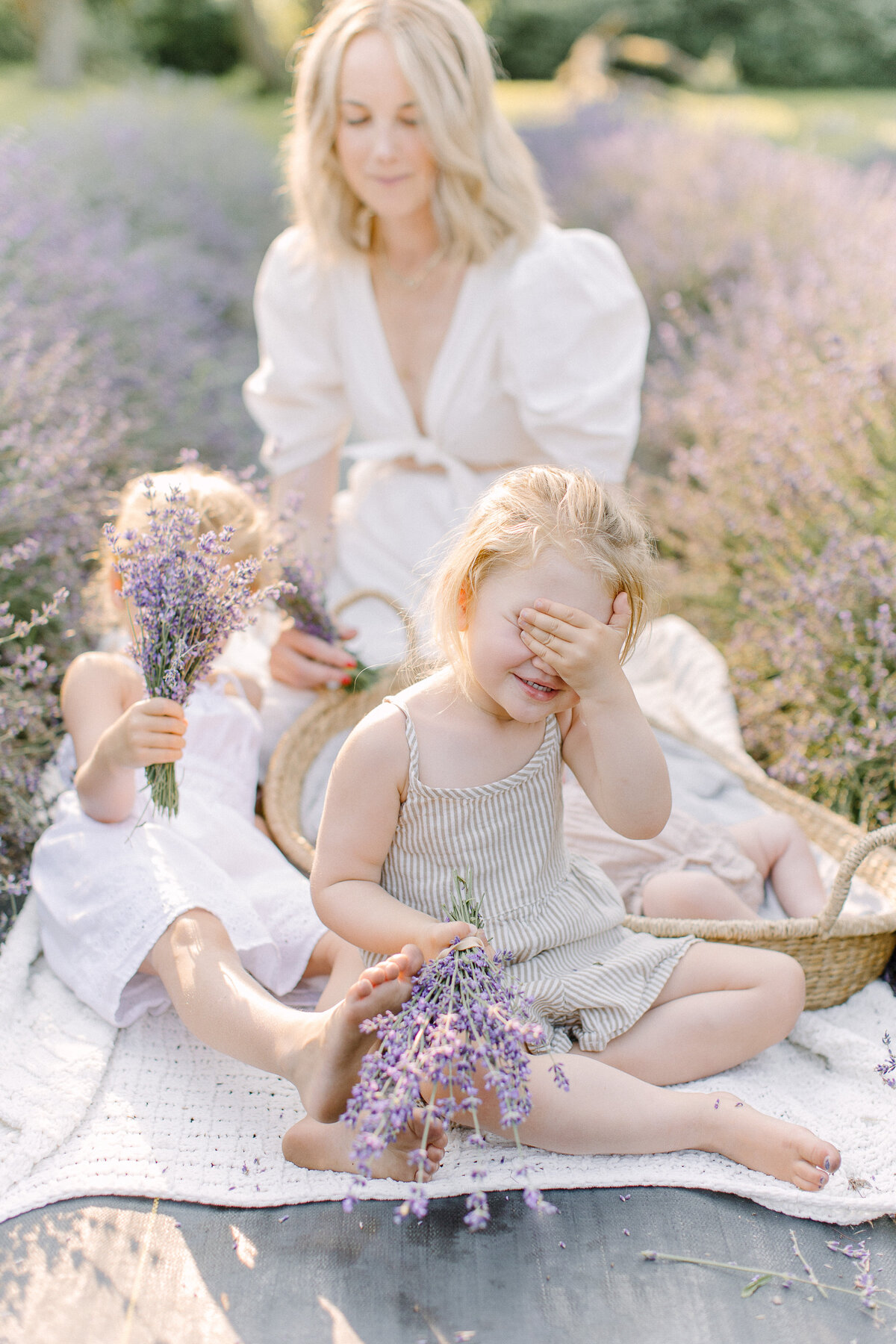A mother and father sit down and hold their baby girl on their lap while the sun is setting in the background creating haze in the photo