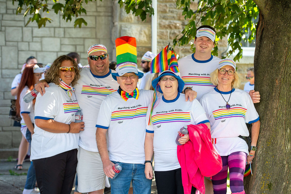 a group of smiling men and women decked out in pride accessories smiling and laughing at the camera.   Captured by Ottawa Event Photographer JEMMAN Photography COMMERCIAL during the Tweed Canopy Growth Pride Parade
