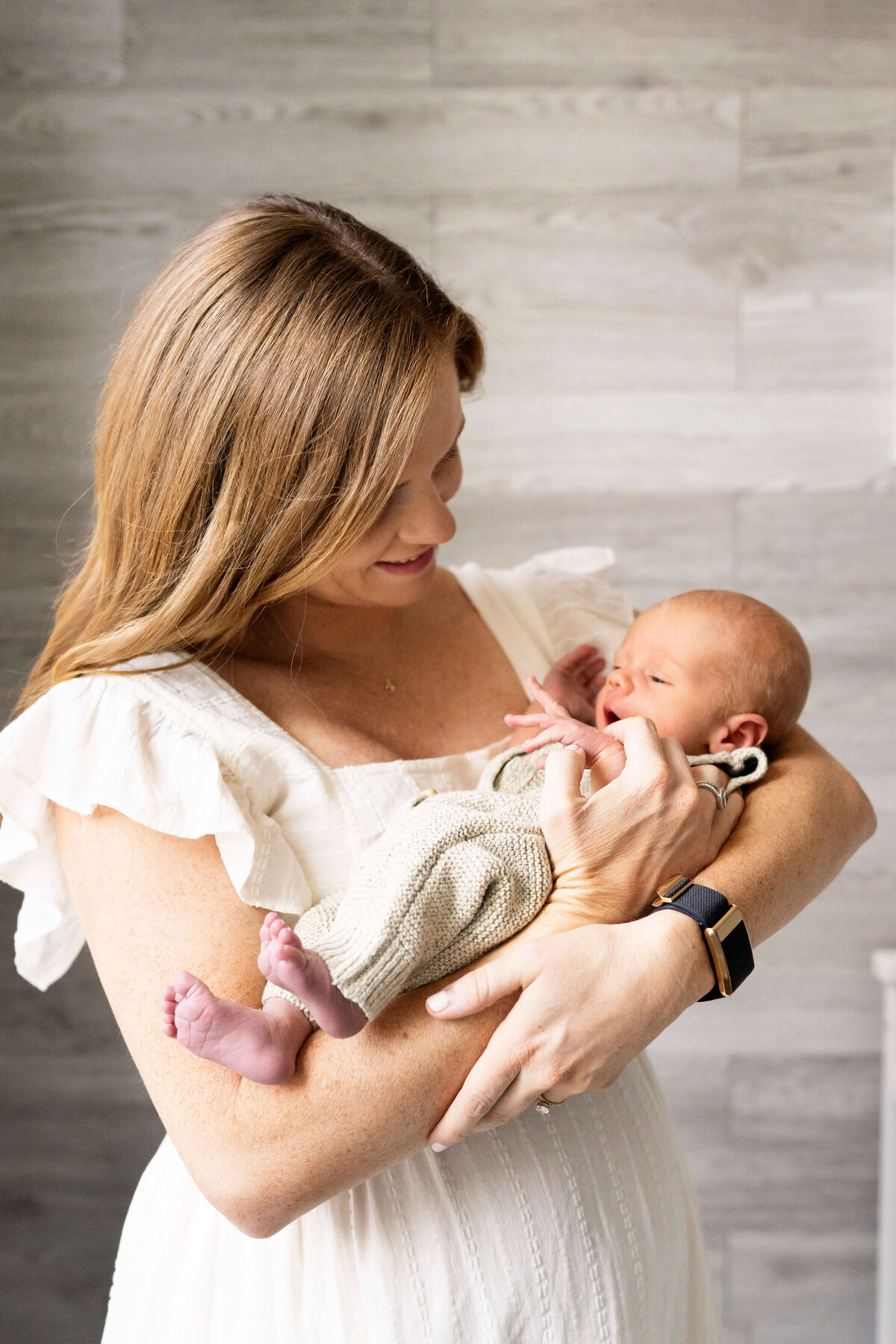 Mother in white dress holding newborn boy during newborn photography session in Atlanta