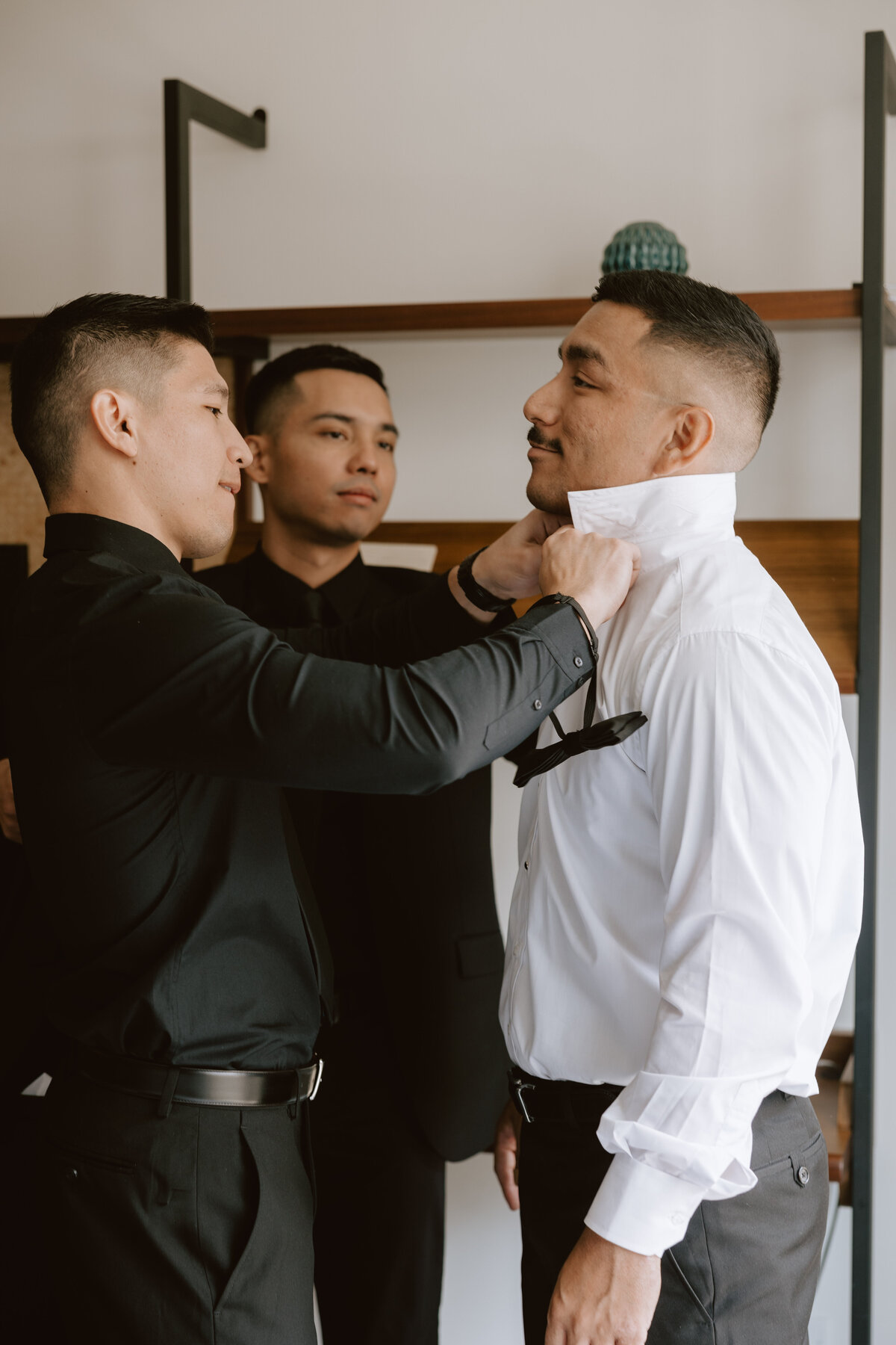 groomsmen helping groom get his bowtie on in a hotel room