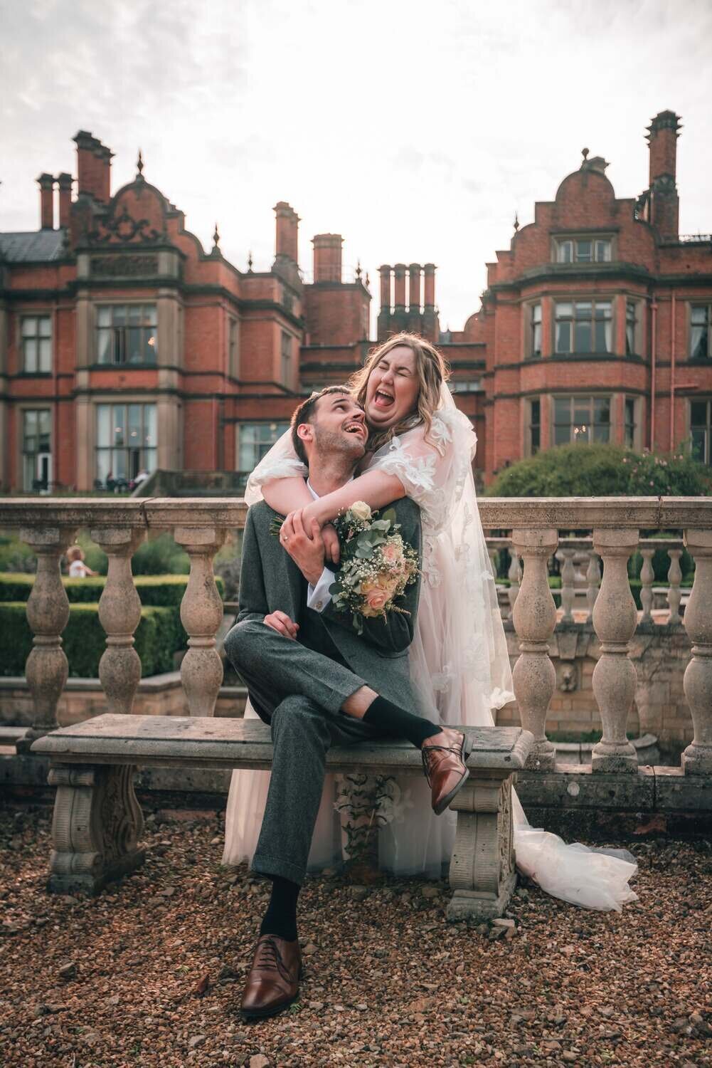 Bride laughs hugging groom sat down outside Welcombe Hotel
