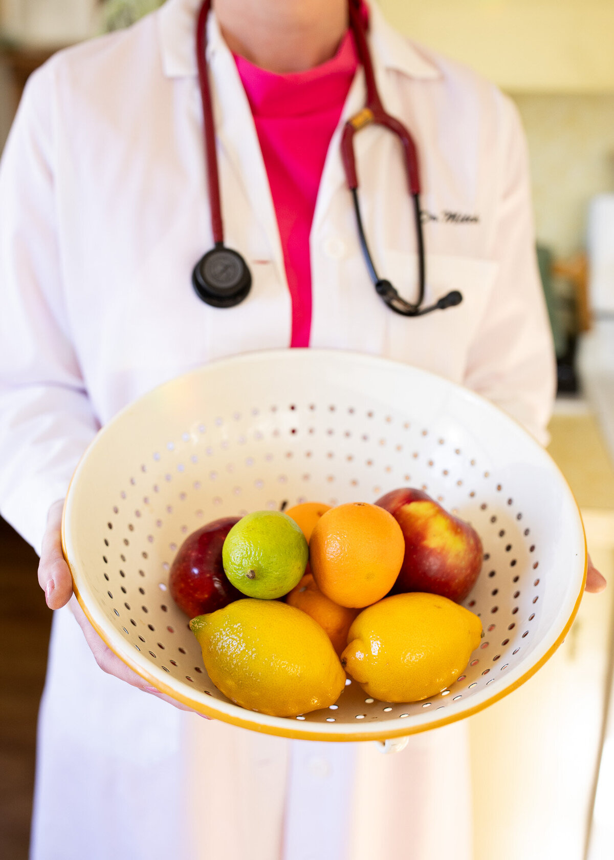 Female physician holds bowl of fruit while wearing a lab coat. 