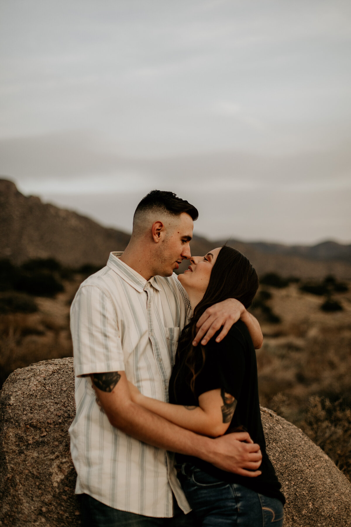 engaged couple holding each other in the desert about to kiss
