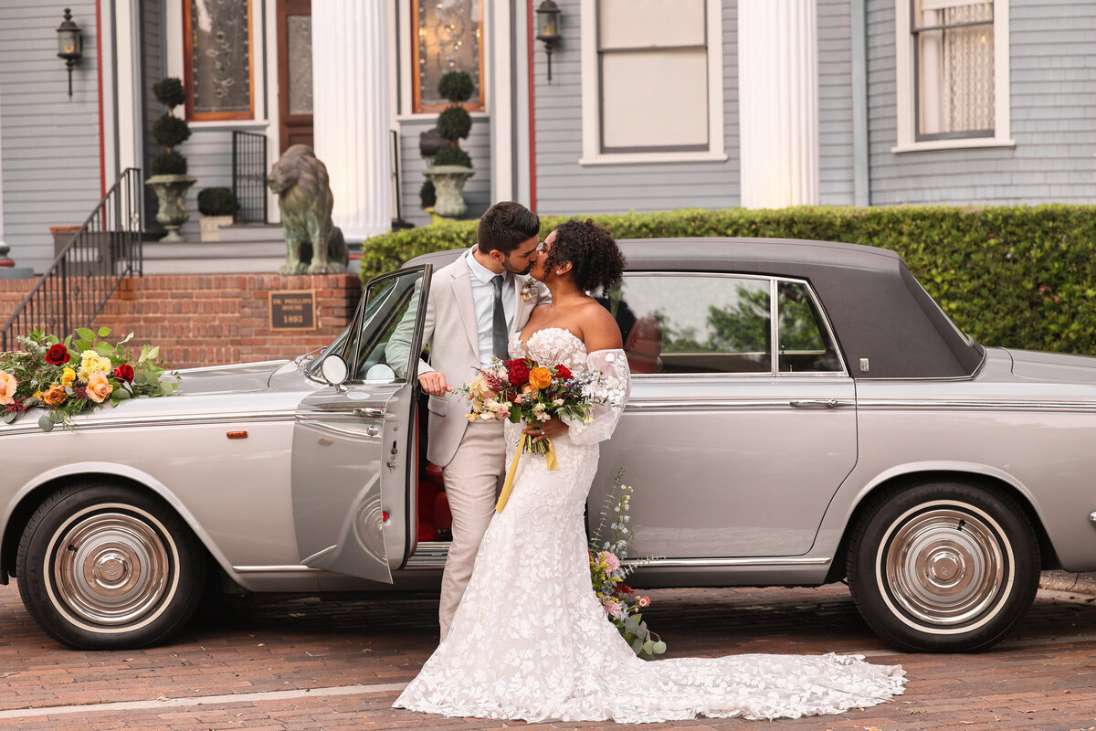 bride wearing lace dress adn groom wearing tan suit kissing in front of gray shiny ventage care