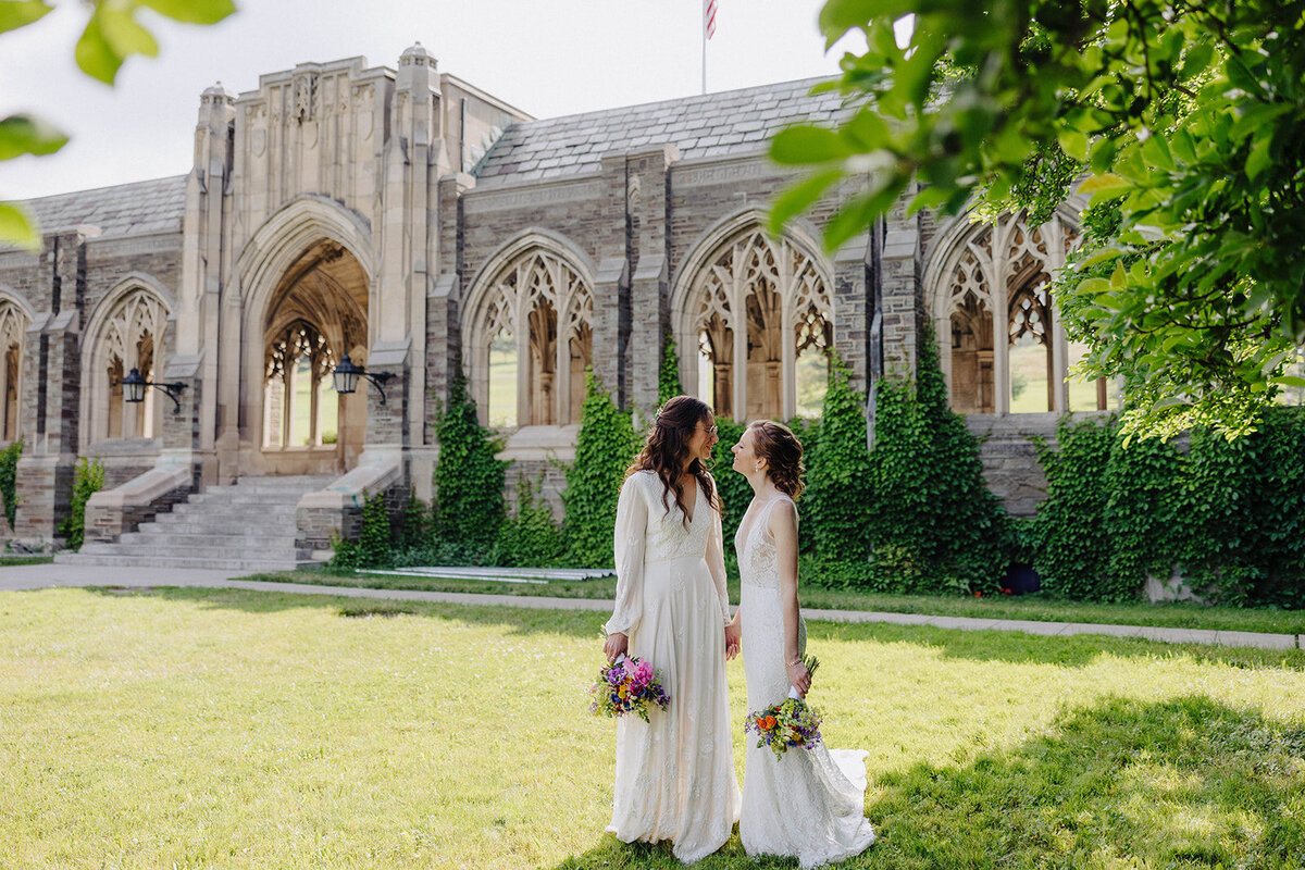 Bride and Bride looking at each other almost kissing under a tree in front of historical building at Cornell University in Ithaca, NY