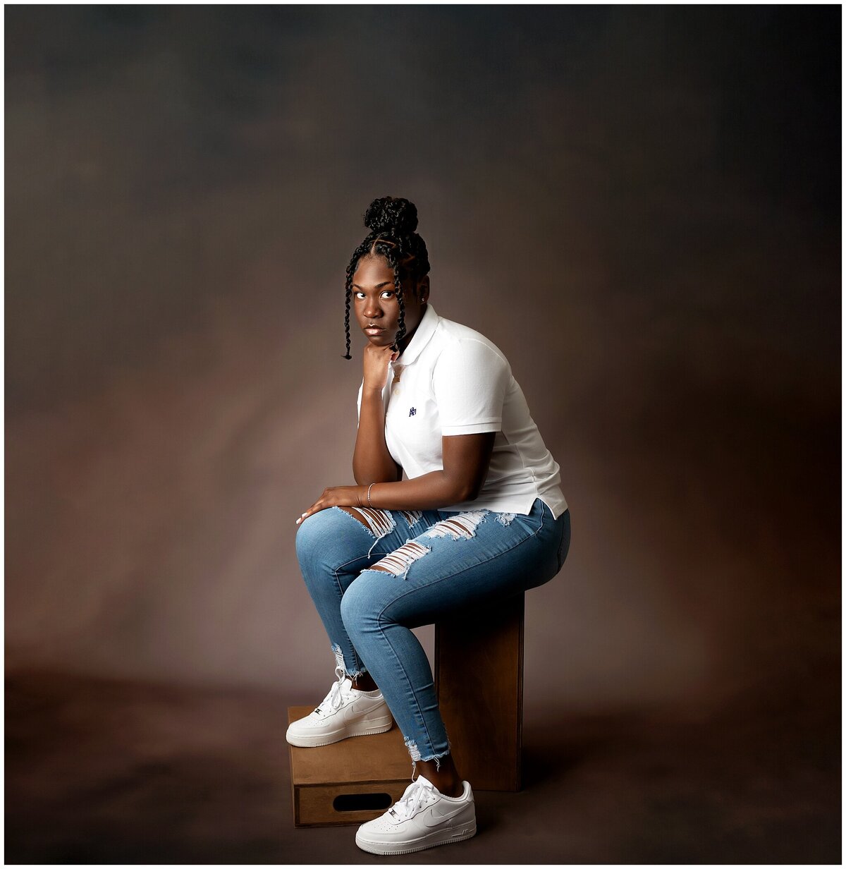 Older child sitting on an apple box with one foot on one box and the other on the floor. She has one hand on her chin and the other hand on her leg.