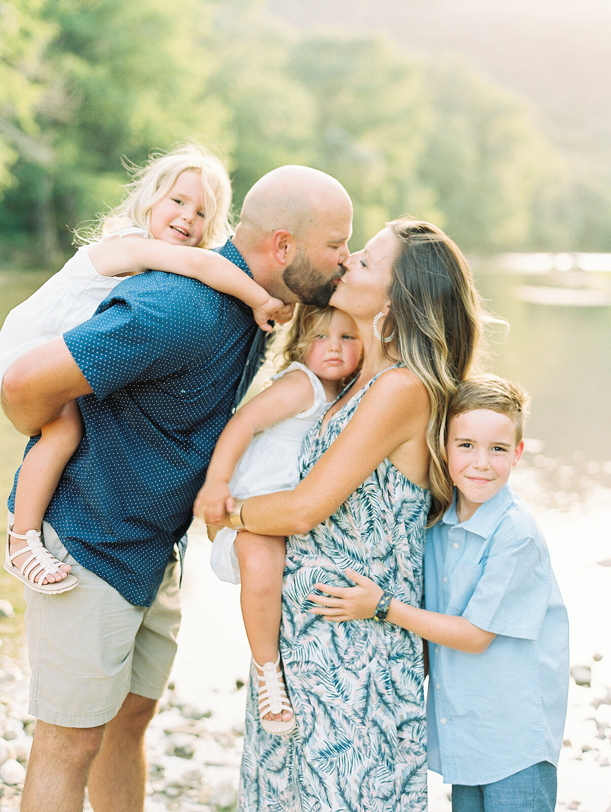 Mom and dad kissing while holding their three children